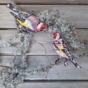Puede incluir: Dos parches bordados de pájaros con patrones de cuadros en rosa, negro, amarillo y azul. Los pájaros están posados en una rama con líquenes grises sobre un fondo de madera. Los pájaros tienen marcas rojas en la cabeza.
