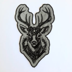 May include: Black embroidered deer head patch with antlers and floral details on a gray fabric background.