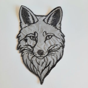 Könnte beinhalten: Ein gestickter Fuchskopf-Patch in Schwarz und Grau. Der Fuchs hat ein detailliertes Gesicht mit einer schwarzen Nase und Schnurrhaaren.