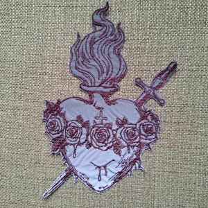 Op de afbeelding: Geborduurde patch met een ontwerp van het Heilig Hart. Het grijze hart is versierd met rozen en doorboord door een zwaard. Boven het hart stijgt een vlam op, alles in grijstinten en bordeaux.