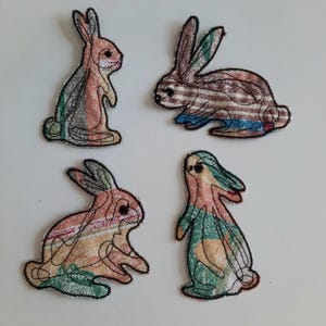 Könnte beinhalten: Vier bunte Stoff-Hasen-Applikationen mit schwarzen Umrissen. Die Hasen sind in verschiedenen Posen und haben unterschiedliche Muster.