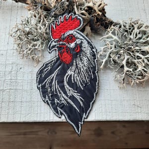 Peut inclure: Patch brodé de coq noir et blanc avec une crête et des barbillons rouges. Le coq est tourné vers la gauche et présente un design détaillé.
