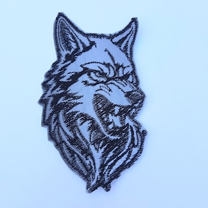 May include: Black and white embroidered patch of a wolf's head with a snarling expression.