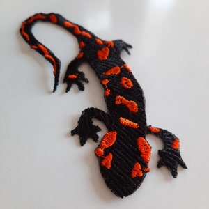 Pu&ograve; includere: Toppa ricamata nera e arancione di una salamandra con la coda arrotolata.