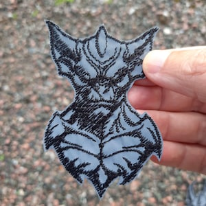 Könnte beinhalten: Schwarzer und grauer gestickter Aufnäher eines Monsters mit scharfen Zähnen und Krallen. Der Aufnäher ist aus Stoff und hat einen gestickten Umriss.