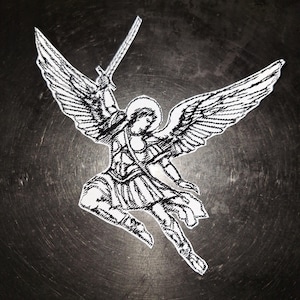 May include: Black and white embroidered patch featuring an angel with large wings, a halo, and a sword raised above its head. The angel is depicted in a dynamic pose, with detailed stitching creating a textured effect.
