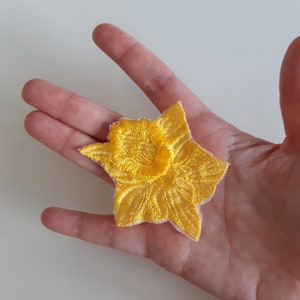Könnte beinhalten: Ein gelber gestickter Narzissenblumen-Patch. Der Patch ist aus Stoff und hat eine weiße Rückseite.