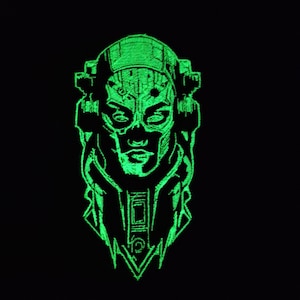 Pode incluir: Um patch bordado verde néon com um rosto estilizado com capacete e design futurista. O patch tem uma aparência detalhada e costurada e está sobre um fundo preto. O design lembra ficção científica ou temas cyberpunk.