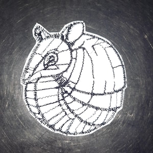 Op de afbeelding: Een zwart-witte lijntekening van een gordeldier dat zich oprolt. De tekening is op een witte achtergrond.