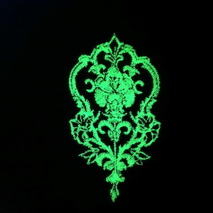 May include: A green glow-in-the-dark floral embroidery design with intricate details. The design features a central flower with swirling leaves and vines.