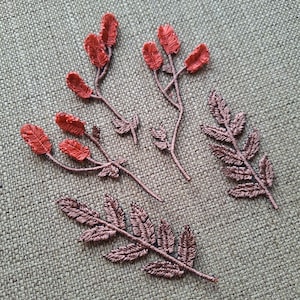 Puede incluir: Cinco aplicaciones de tela bordada, dos con ramas de hojas marrones y tres con capullos de flores rojas y tallos marrones.