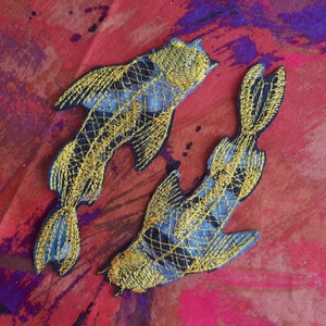 Op de afbeelding: Twee geborduurde vispatches in zwart en goud. De vissen zijn gestileerd en hebben een gedetailleerd ontwerp. De patches zijn perfect om kleding, tassen of andere accessoires een unieke touch te geven.