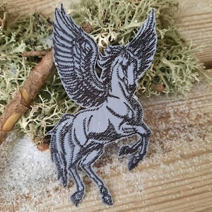 Peut inclure: Un écusson brodé noir et gris à repasser représentant un cheval ailé, ou pégase, avec ses ailes déployées.