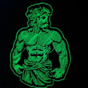 May include: A green glow-in-the-dark embroidered patch of a muscular figure with a crown of leaves on their head.