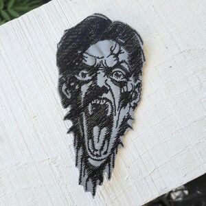 May include: Black and white embroidered iron-on patch of a screaming face with a jagged, uneven edge.