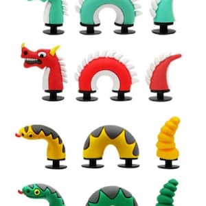 May include: A collection of colorful, cartoonish shoe charms in the shape of dragons and snakes. The charms are in various colors, including blue, green, red, yellow, and pink. Each charm has a black base.