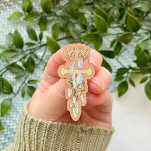 Könnte beinhalten: Eine hölzerne Schwertpins mit floralem Design. Das Schwert ist in Gelb-, Grün- und Rosatönen bemalt. Die Blumen sind in Blau-, Rosa- und Weißtönen bemalt.