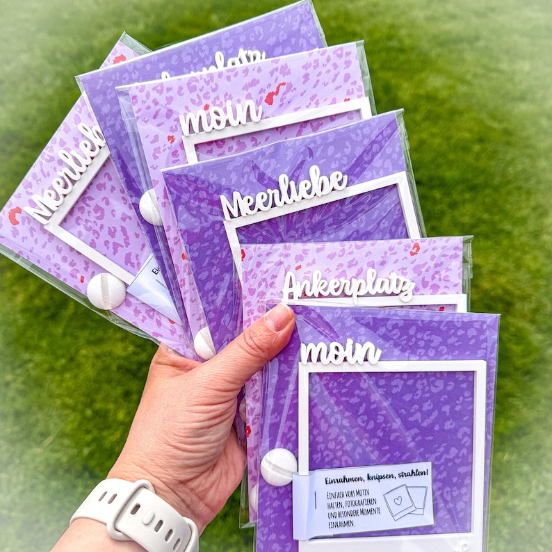 May include: A collection of purple photo frames with white accents and text. The frames have a leopard print design and the words "Meerlieb", "moin", and "Ankerplatz" are visible. The frames are held together with a white ball and are in a clear plastic sleeve.