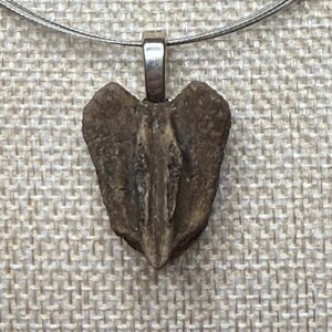May include: A heart-shaped pendant necklace with a silver-colored bail and a brown, textured stone. The pendant hangs from a multi-strand silver-colored wire necklace.