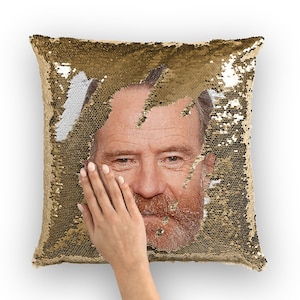May include: A gold sequin pillow with a man's face peeking out from the center. The face is visible when the sequins are flipped to reveal a white background.