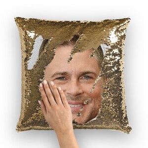 Könnte beinhalten: Ein Kissen aus goldenen Pailletten, aus dessen Mitte ein Männergesicht hervorlugt. Die Pailletten sind reversibel, und das Gesicht wird sichtbar, wenn die Pailletten umgedreht werden.