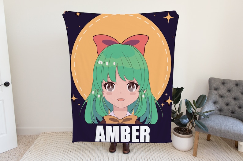 May include: A blue and purple blanket with a cartoon illustration of a girl with green hair and a red bow. The girl is surrounded by a yellow circle with stars. The text "AMBER" is printed in white below the girl.