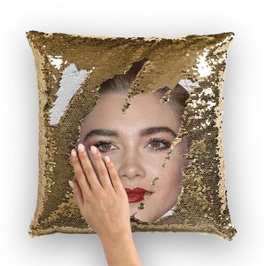 Puede incluir: Una almohada de lentejuelas doradas con la cara de una mujer asomando por las lentejuelas. La mujer tiene el pelo castaño, los ojos marrones y los labios rojos.