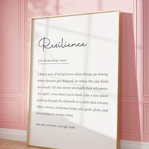 May include: A framed print with the definition of "Resilience" in elegant script. The definition is written in black text on a white background, with a gold frame. The print is leaning against a pink wall.