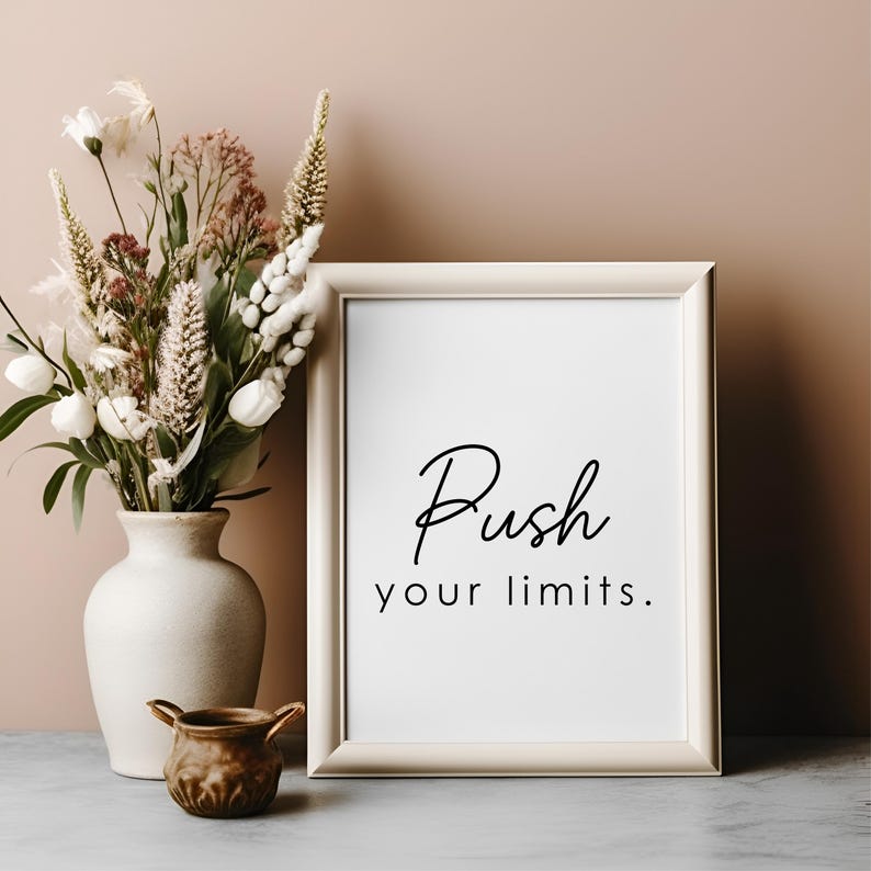 May include: A white framed print with the text "Push your limits." on a white background. The print is sitting on a table next to a vase with dried flowers.