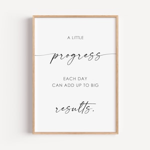May include: A framed print with a white background and black text. The text reads "A little progress each day can add up to big results." The frame is a light brown color.