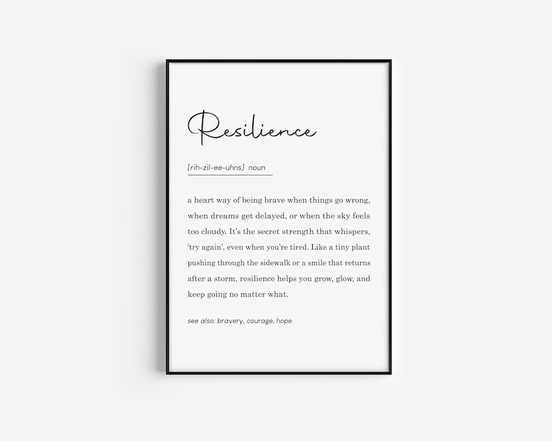 May include: A framed print with the word "Resilience" in elegant script. Below, a definition explains resilience as a way of being brave. The black frame surrounds a white background with black text, suitable for home or office decor.
