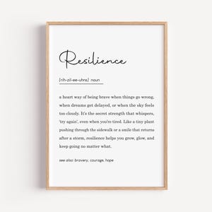 May include: A framed print with the definition of "Resilience" in black text on a white background. The definition includes the pronunciation and a description of resilience. The frame is a light brown color.