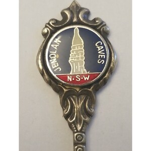 May include: Silver souvenir spoon with a blue and red enamel design. The spoon features a depiction of Jenolan Caves, N.S.W.