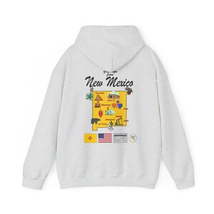 Pode incluir: Uma camisa de moletom cinza com capuz com uma estampa gráfica de um mapa do Novo México. O mapa apresenta vários marcos e cidades, incluindo Albuquerque, Santa Fe e Las Cruces. O texto "Greetings from New Mexico" é impresso acima do mapa.