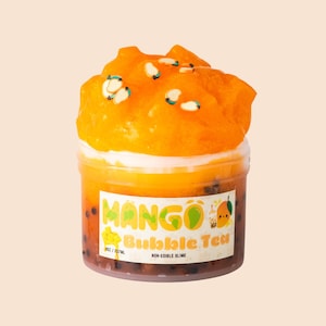 May include: A clear plastic container filled with orange-coloured non-edible slime, resembling mango bubble tea. The container has a white rim and is topped with a fluffy orange substance and decorative sprinkles. The label reads "Mango Bubble Tea".