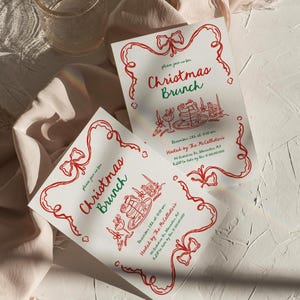 May include: Two white Christmas Brunch invitations with red and green text and illustrations. The invitations have a red ribbon border and include the date, time, and host information. A glass and fabric are in the background.