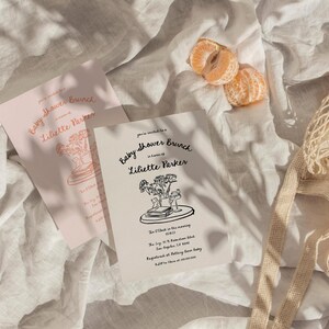 May include: A white card with black text announcing a baby shower brunch for Liliette Parker. The card features a line drawing of a bouquet of flowers and a stack of books on a tray.