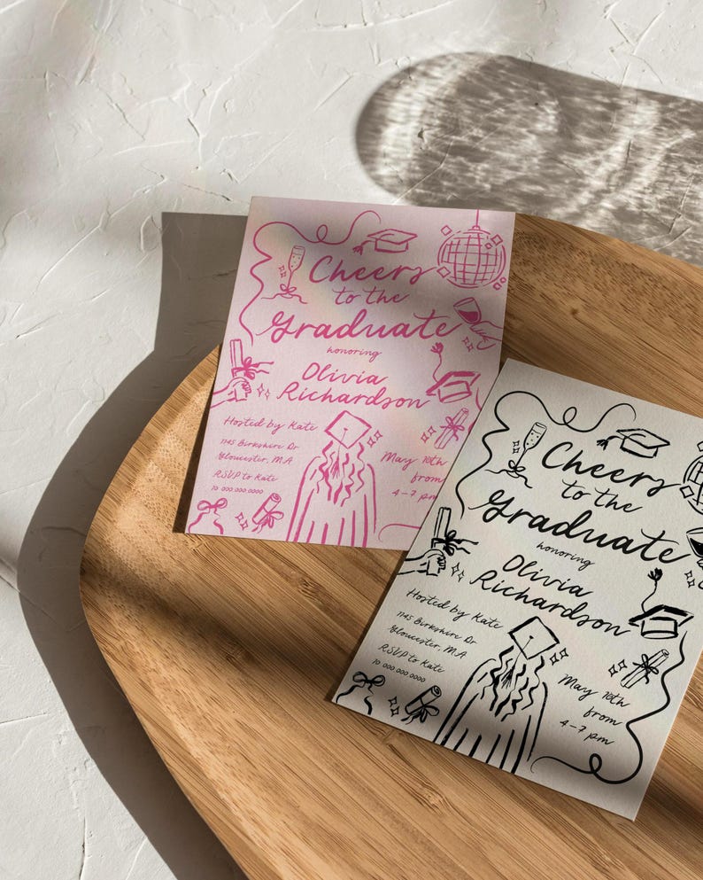 Puede incluir: Dos invitaciones a una fiesta de graduaci&oacute;n con dibujos a tinta negra y rosa de un graduado con birrete y toga, un diploma y otras im&aacute;genes con tem&aacute;tica de graduaci&oacute;n. Las invitaciones dicen "Cheers to the Graduate" e incluyen el nombre "Olivia Richardson". Las invitaciones est&aacute;n sobre una superficie de madera.