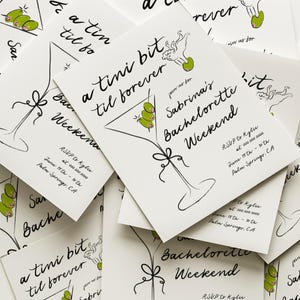 May include: A stack of white cards with black calligraphy that reads "a tini bit til forever" and "Sabrina's Bachelorette Weekend". The cards feature a martini glass with olives and a bow. RSVP information is included on the cards.