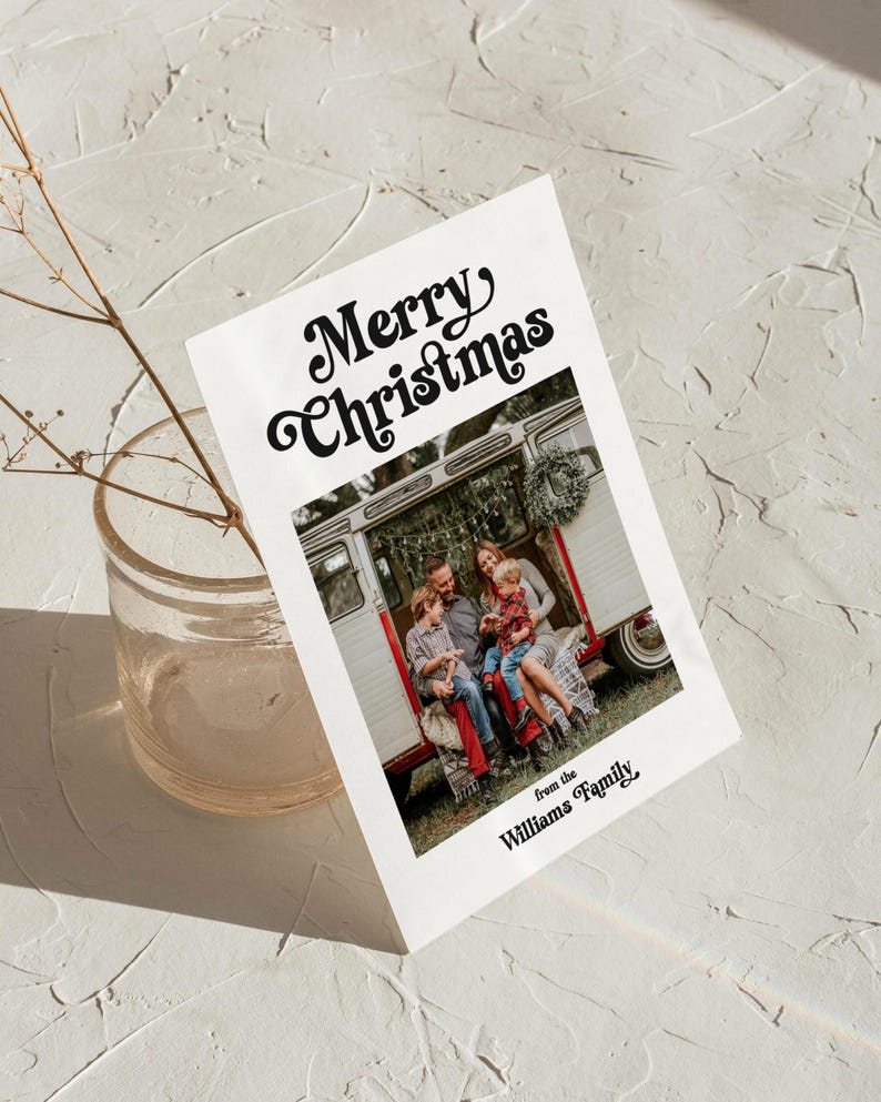 May include: A white Christmas card with the text "Merry Christmas" in a retro font. The card features a family photo in front of a vintage camper. The text "from the Williams Family" is printed below the photo.