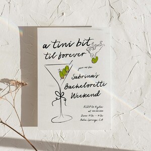 May include: A black and white illustration of a martini glass with olives, with the text "a tini bit til forever" and "Sabrina's Bachelorette Weekend" on a white background. The text also includes RSVP information, date, and location.
