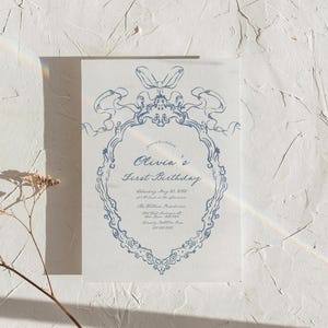 May include: A blue and white invitation card with a decorative border and the text "Olivia's First Birthday" with the date and time of the party.