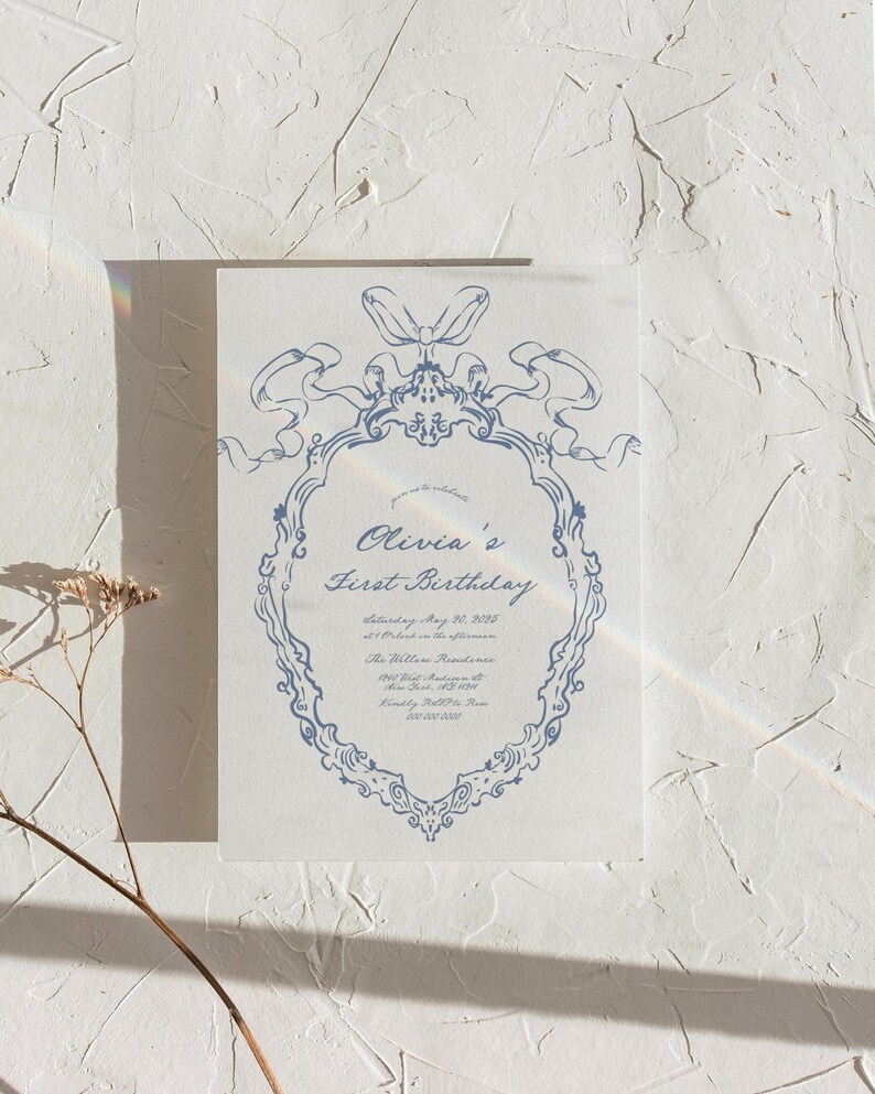 May include: A blue and white invitation card with a decorative border and the text "Olivia's First Birthday" with the date and time of the party.