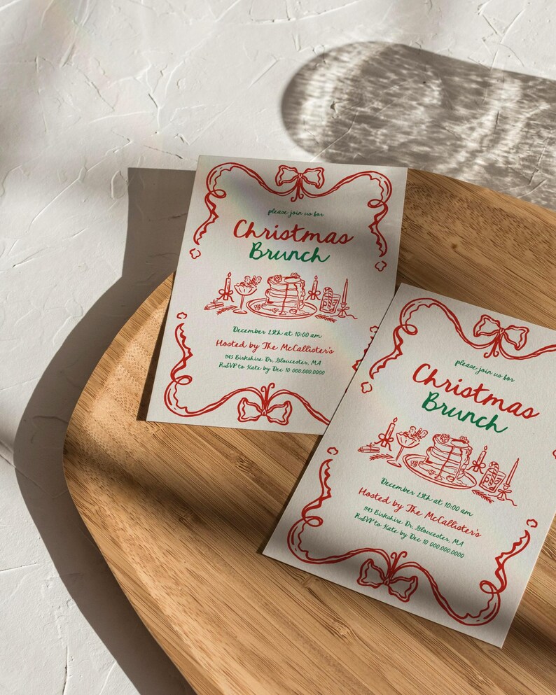 May include: Two Christmas Brunch invitations on a wooden tray. The invitations have a red and green design with the words "Christmas Brunch" and event details. The invitations are decorated with festive illustrations.