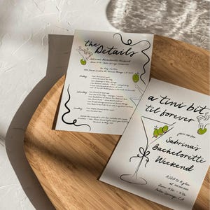 May include: A white card with black calligraphy text that reads "a tini bit til forever" and "join us for Sabrina's Bachelorette Weekend". The card also features a line drawing of a martini glass with olives. The text "RSVP to Kylie at 000-200-0000 June 17th - 20th Palm Springs, CA" is also included.