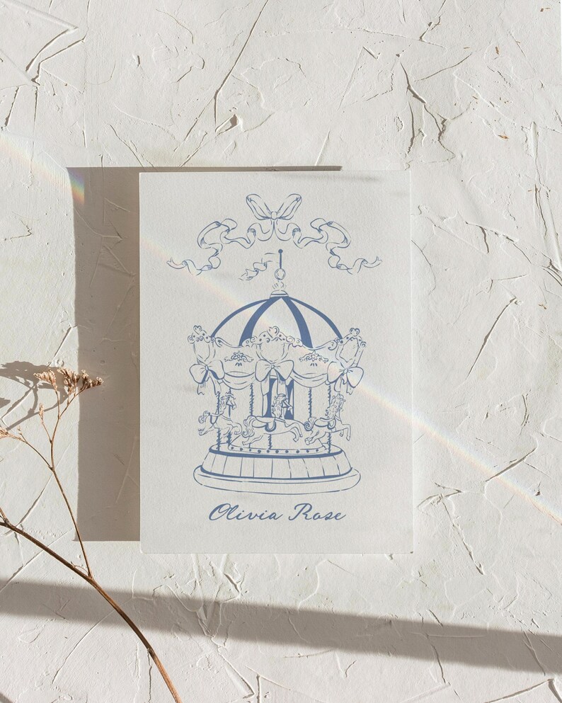 May include: A blue and white illustration of a carousel with a ribbon and bow at the top. The text "Olivia Rose" is printed below the carousel.