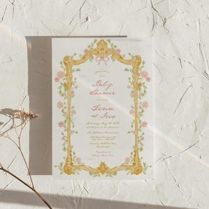 May include: A baby shower invitation with a gold ornate frame decorated with pink and green flowers. The text reads "Please join us for a Baby Shower honoring Finn of Iris Saturday, May 21, 2023 at 2 PM in the afternoon The Willow Residence 123 Main Street Anytown, USA RSVP by May 15th Registered at Baby Gear Store"