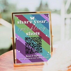 May include: A gold-framed sign with a rainbow striped background and a butterfly graphic. The sign says "share your sparkling shots" and includes a QR code with the text "Scan & Upload your photos to our online album".
