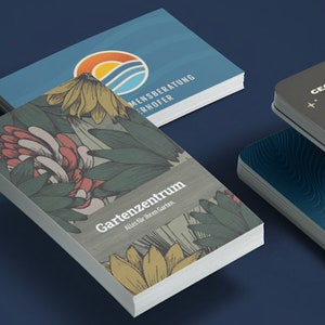 Puede incluir: Tres tarjetas de visita con diseños diferentes. La primera tarjeta es azul con un logotipo de sol y ola y el texto "Mensberatung Erhoffer". La segunda tarjeta tiene un diseño floral con el texto "Gartenzenrum Alles fur Ihren Garten". La tercera tarjeta es gris con un logotipo de estrella y luna y el texto "Ananda Yoga".