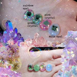 May include: The image showcases a collection of colorful crystal-themed items. The text "crystal cavern" is at the top. There are several crystal formations and small, oval-shaped gems labeled "rainbow opal," "green crystal," "pink crystal," and "milk opal."